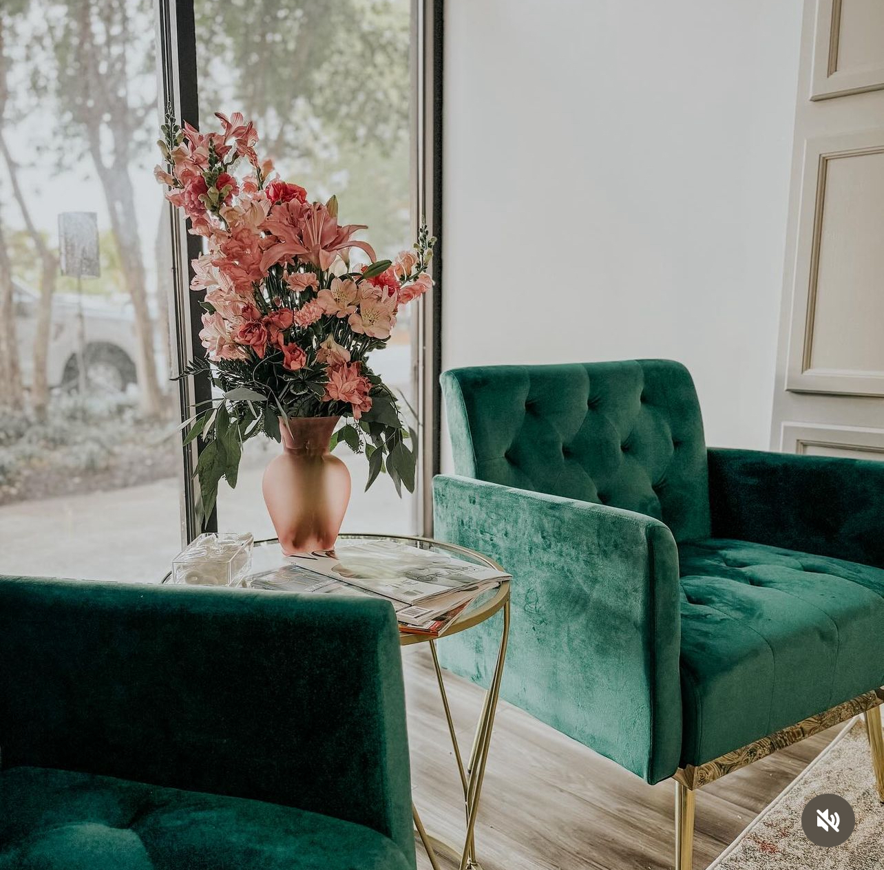 Green velvet armchairs and a vase of pink flowers beside a window